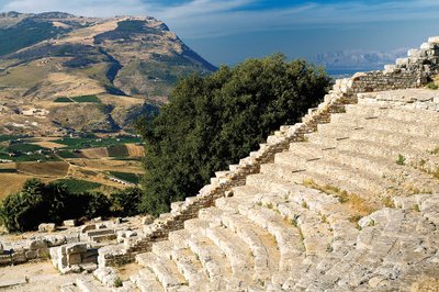 Ein altes Amphitheater mit gut erhaltenen Steinstufen, umgeben von üppigen grünen Feldern und majestätischen Bergen.