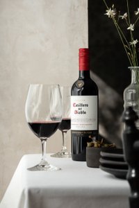 Eine Flasche Casillero del Diablo Cabernet Sauvignon steht neben zwei Weingläsern auf einem weißen Tisch, umgeben von eleganten Details.